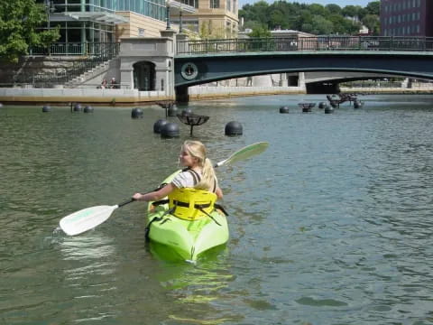 a man in a kayak in a river with a bridge and buildings