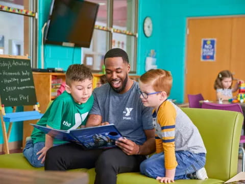 a man and two boys sitting on a green chair in a classroom