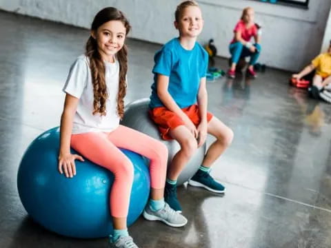 a person and a boy sitting on a ball in a gym