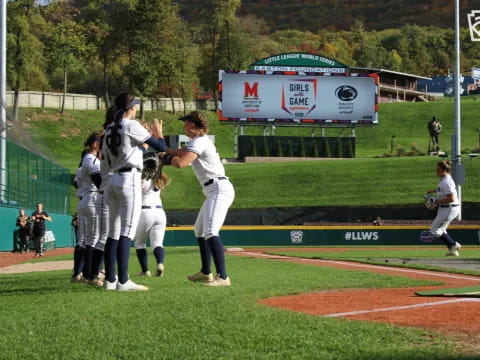 a group of girls in white uniforms on a baseball field