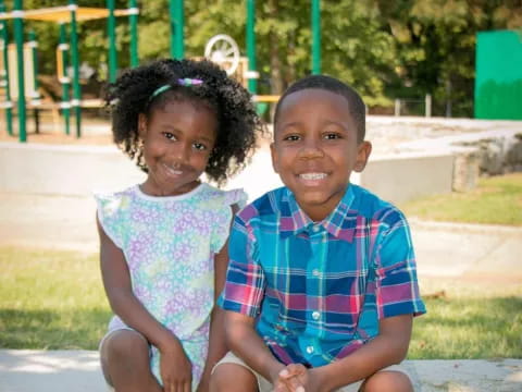 a boy and girl sitting on a bench in a playground