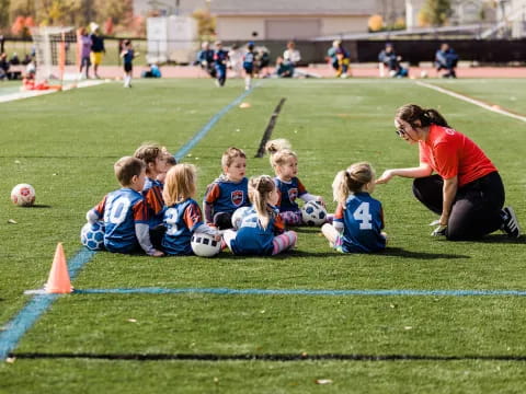 a person kneeling next to a group of kids playing football