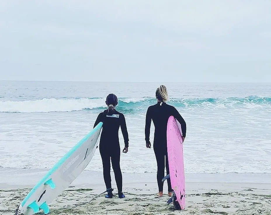 a couple of people stand on a beach with surfboards