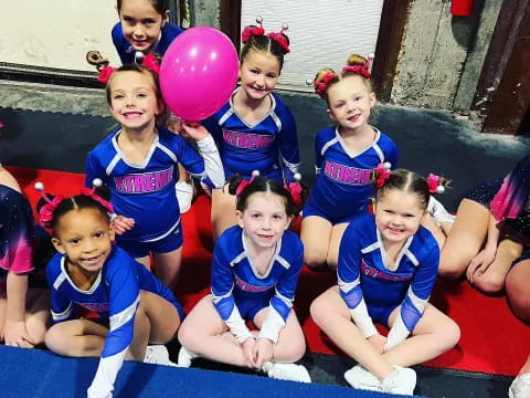 a group of girls in blue and red uniforms with a pink balloon