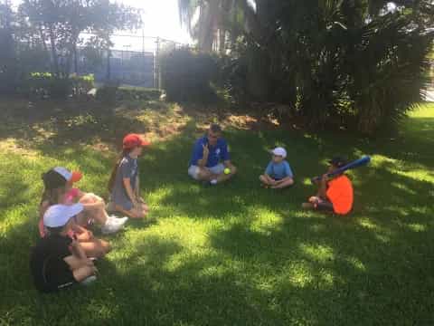 a group of kids sitting on the grass with baseball bats