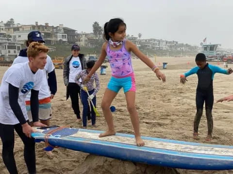 a group of kids playing on a surfboard at the beach
