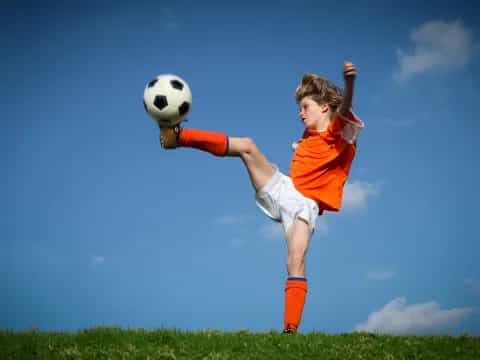 a boy jumping to kick a football ball