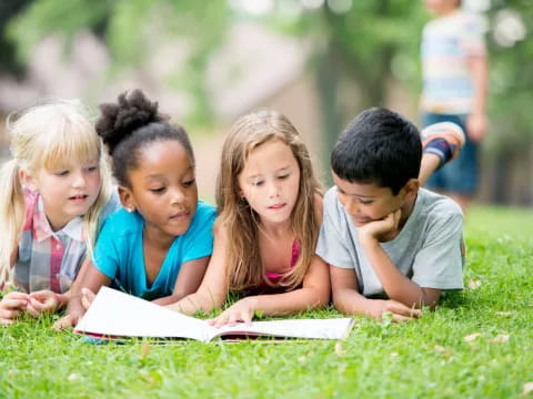 a group of children sitting on the grass looking at a book