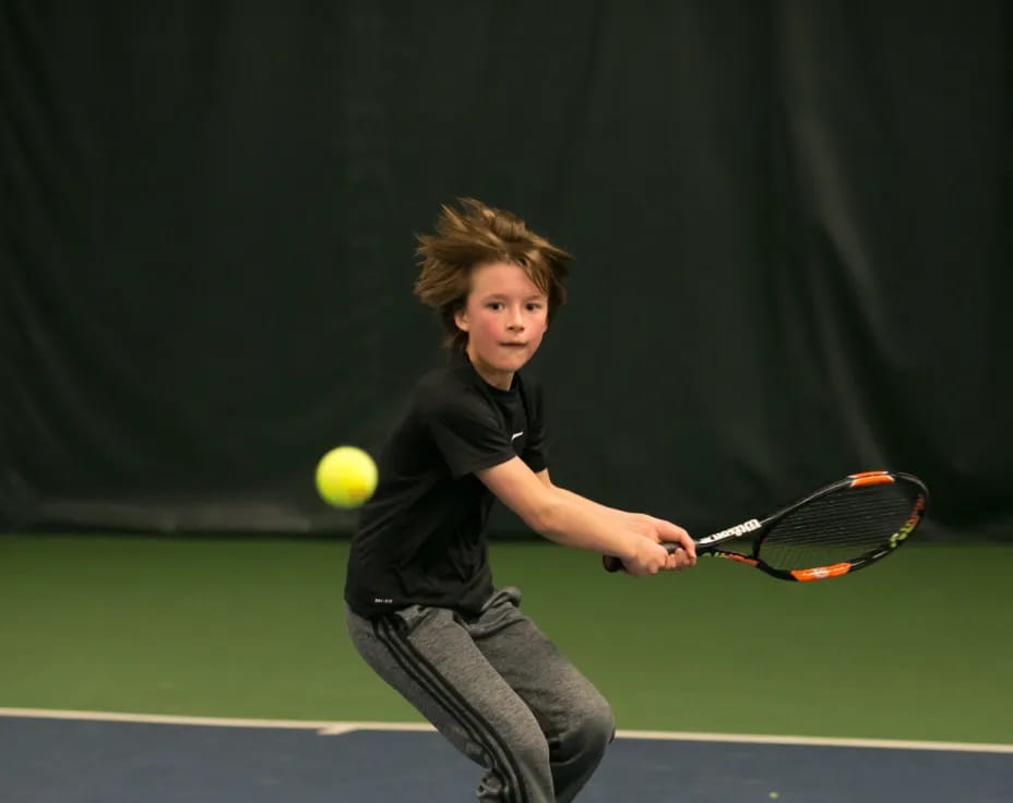 a boy hitting a ball with a tennis racket