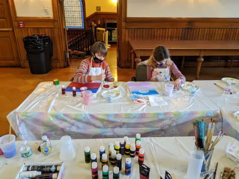 a couple of girls sitting at a table with paintbrushes and paint brushes