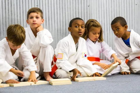 a group of children in white karate uniforms sitting on the floor