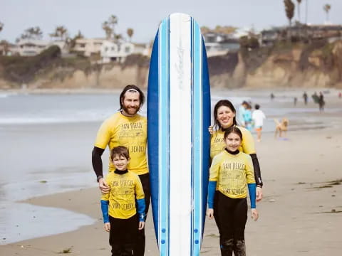 a group of kids stand on the beach with a surfboard