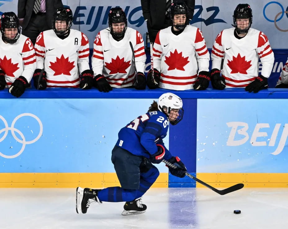 a hockey player in blue and white with a hockey stick in front of a group of people in