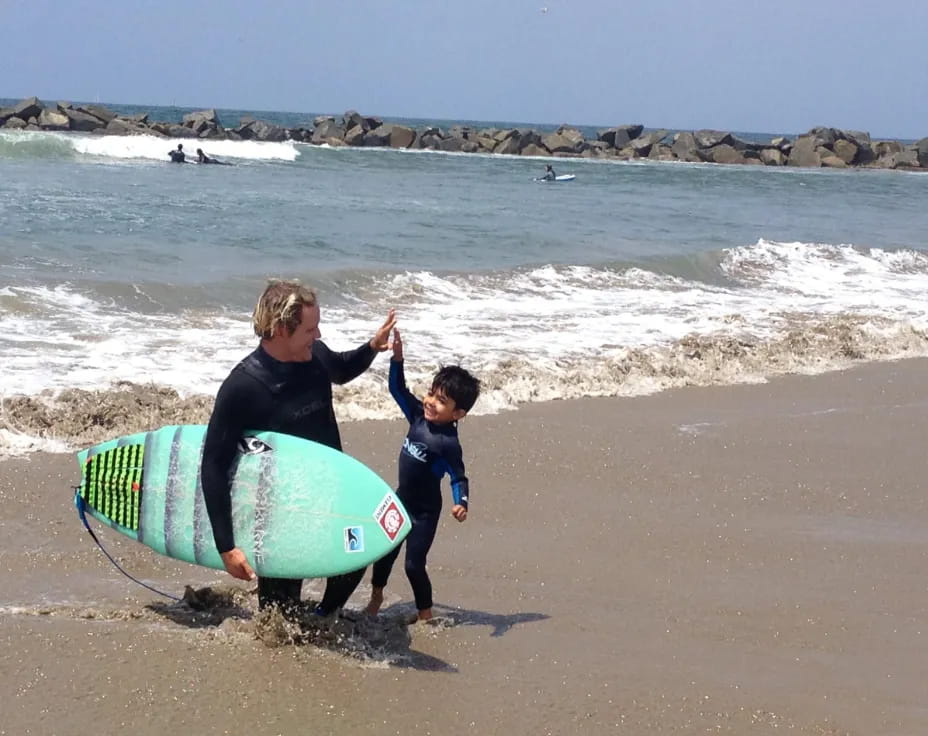 a person and a boy carrying surfboards on a beach