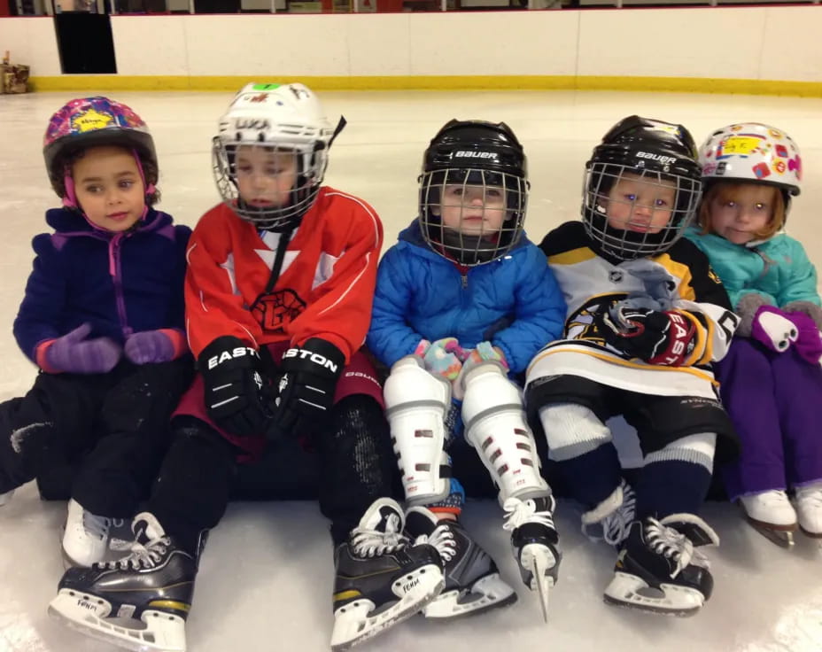 a group of kids wearing helmets and sitting on ice