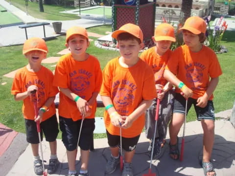 a group of kids wearing orange shirts and holding shovels