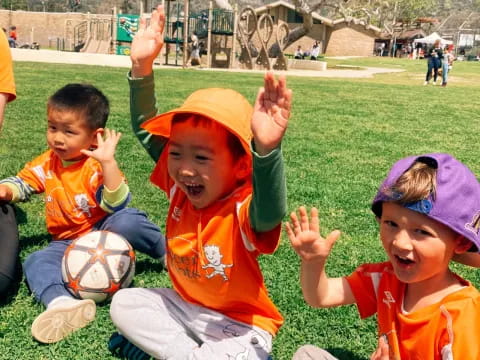 a group of kids sitting on the grass with their hands up