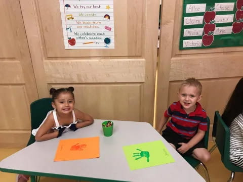 a couple of kids sitting at a table with a paper and a sign