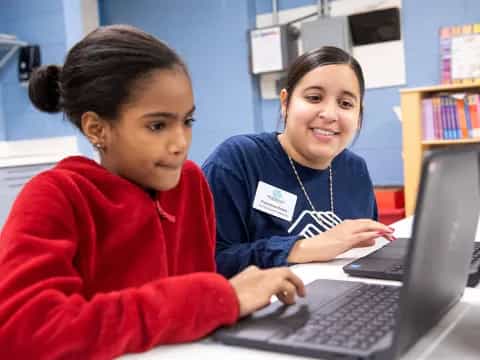 a person and a young girl looking at a laptop