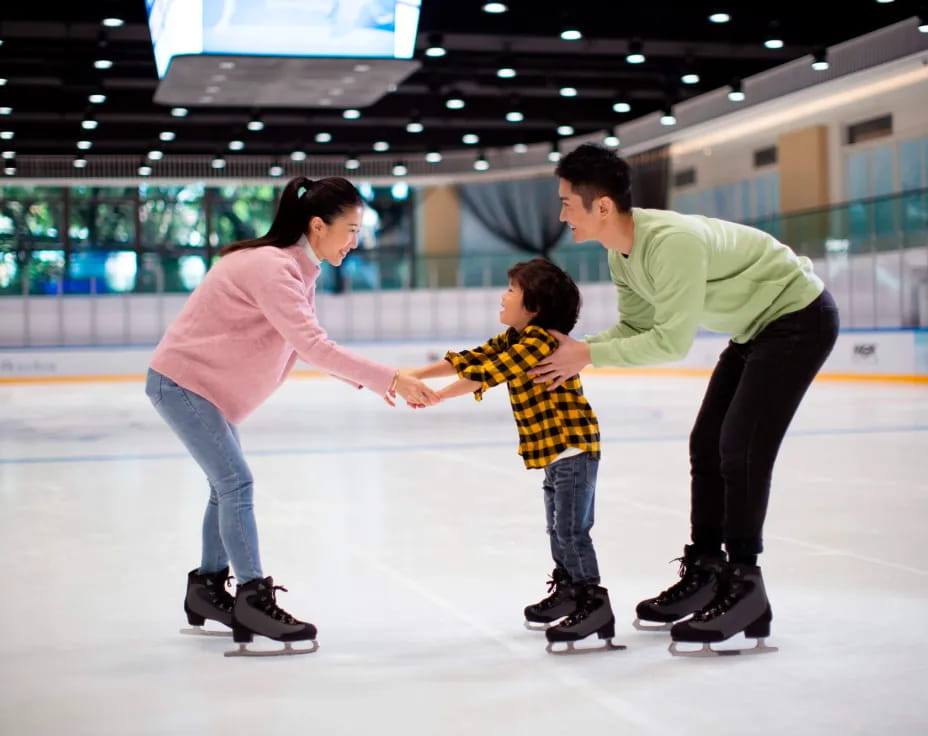a man and woman holding hands with a child on an ice rink