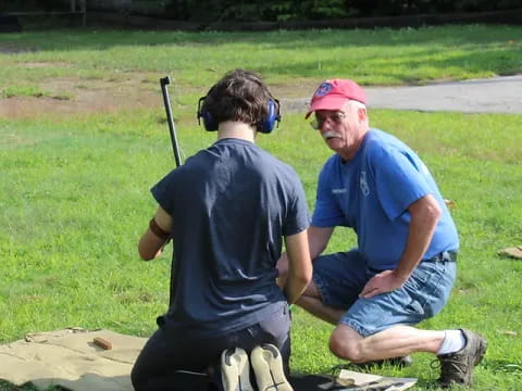 a couple of men sitting on the grass with a backpack and a helmet