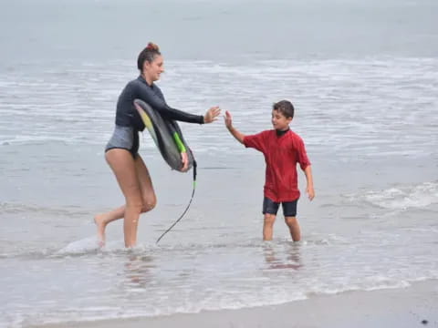 a man and a boy playing with a surfboard on the beach