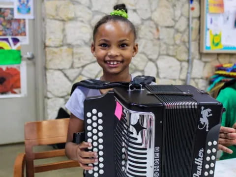a young girl holding a large black accordion