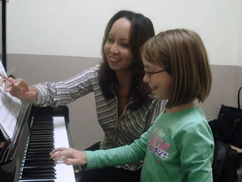a woman playing a piano with another woman holding a pen
