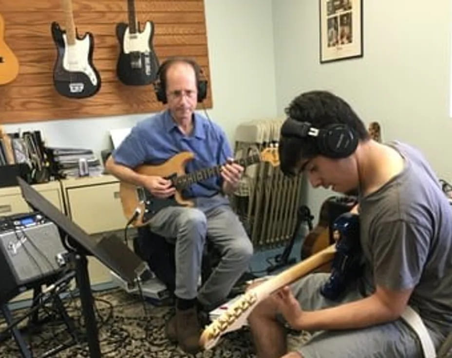 a man playing guitar next to a man wearing headphones