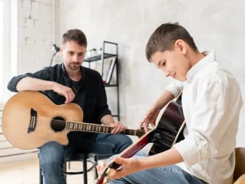 a man playing a guitar next to a man sitting on a chair