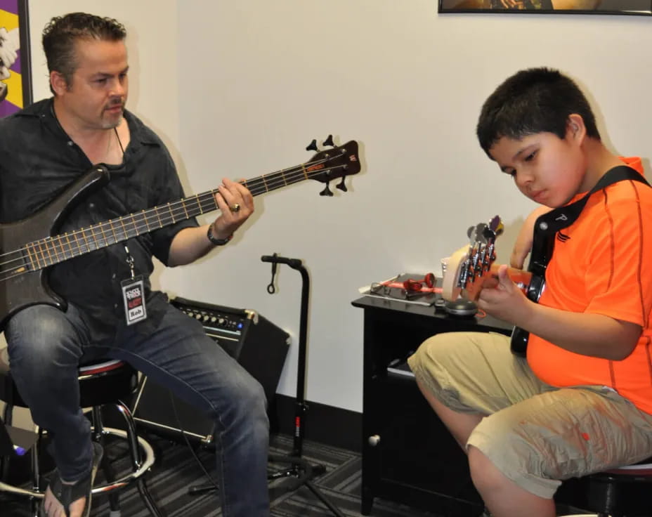 a man playing guitar next to a boy sitting on a stool