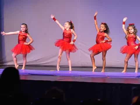 a group of girls in red dresses jumping on a stage