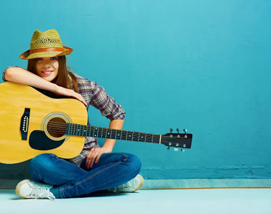 a young girl sitting on the floor playing a guitar