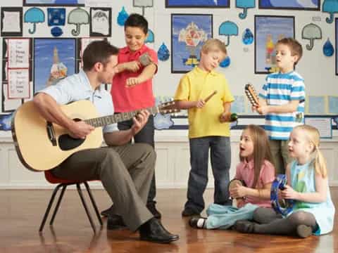 a person playing guitar in front of a group of children