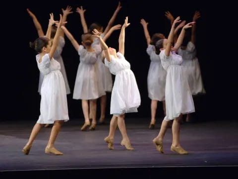a group of girls in white dresses dancing on a stage