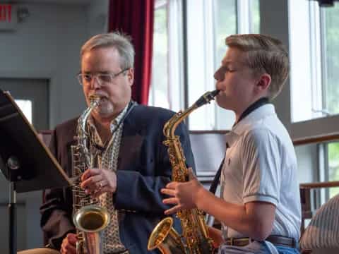 a man playing a saxophone next to a boy playing a saxophone