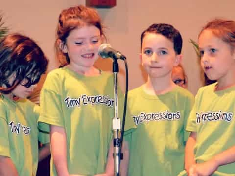 a group of kids in green t-shirts standing in front of a microphone