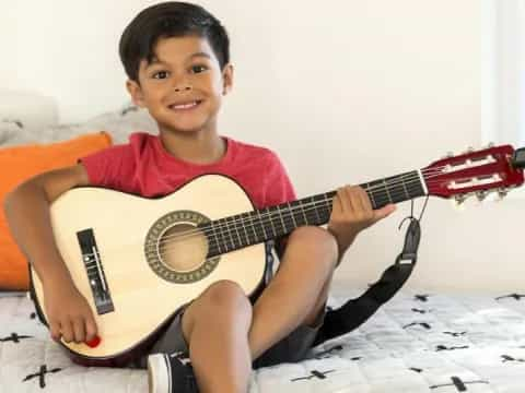 a boy sitting on a bed playing a guitar