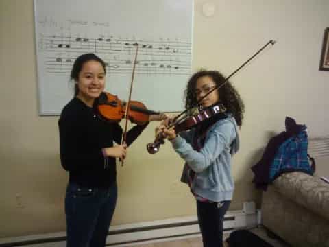 a person playing a violin next to a girl playing a violin