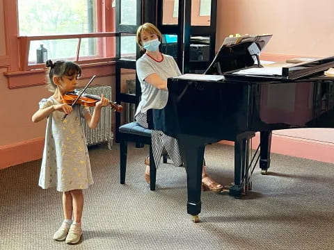 a girl playing a violin next to a person in a white dress