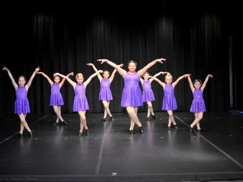 a group of girls in purple dresses dancing on a stage