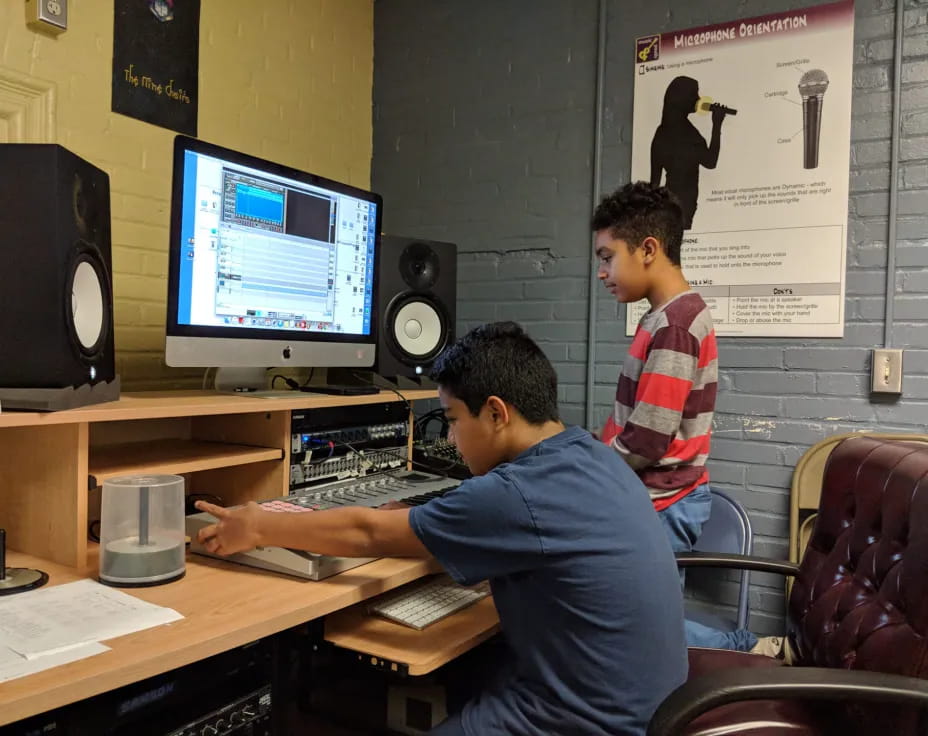 a couple of men sitting at a desk with a computer and speakers