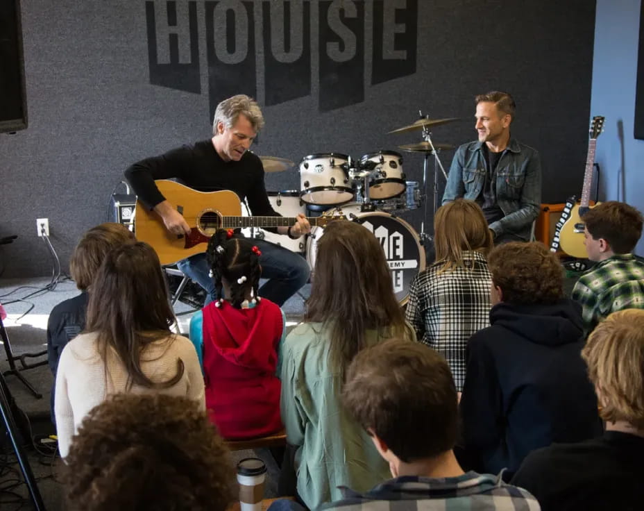 a group of people sitting in a room with a person standing in front of a microphone