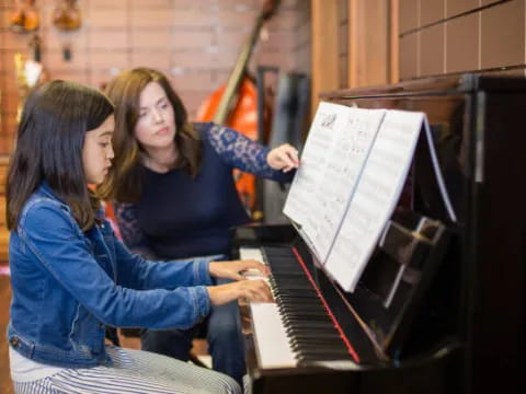 a person playing a piano with another woman holding a paper