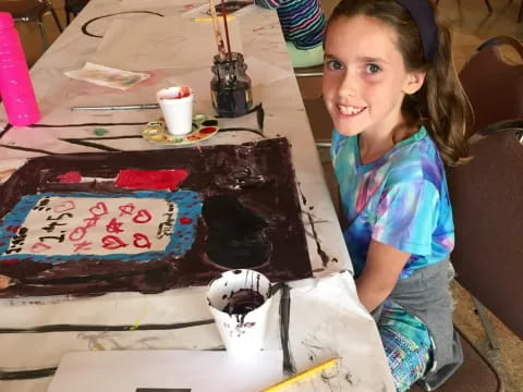 a girl sitting at a table with a cake and a doll