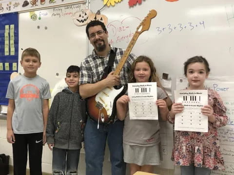 a person holding a guitar with children standing next to him