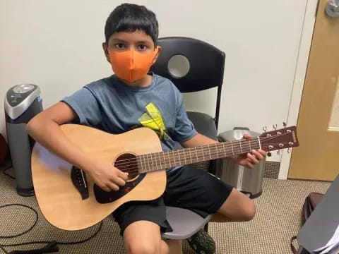 a boy sitting on a chair playing a guitar
