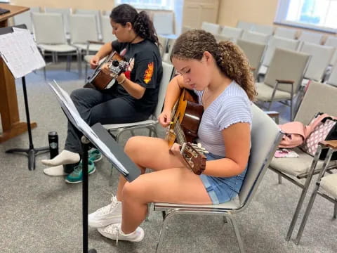 a person playing a guitar next to a person sitting in a chair