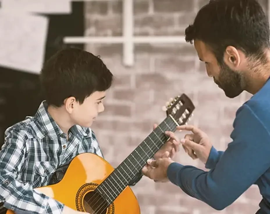 a man playing a guitar to a young boy