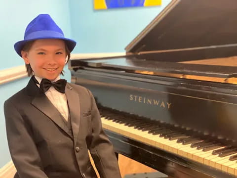 a boy in a suit and hat playing a piano